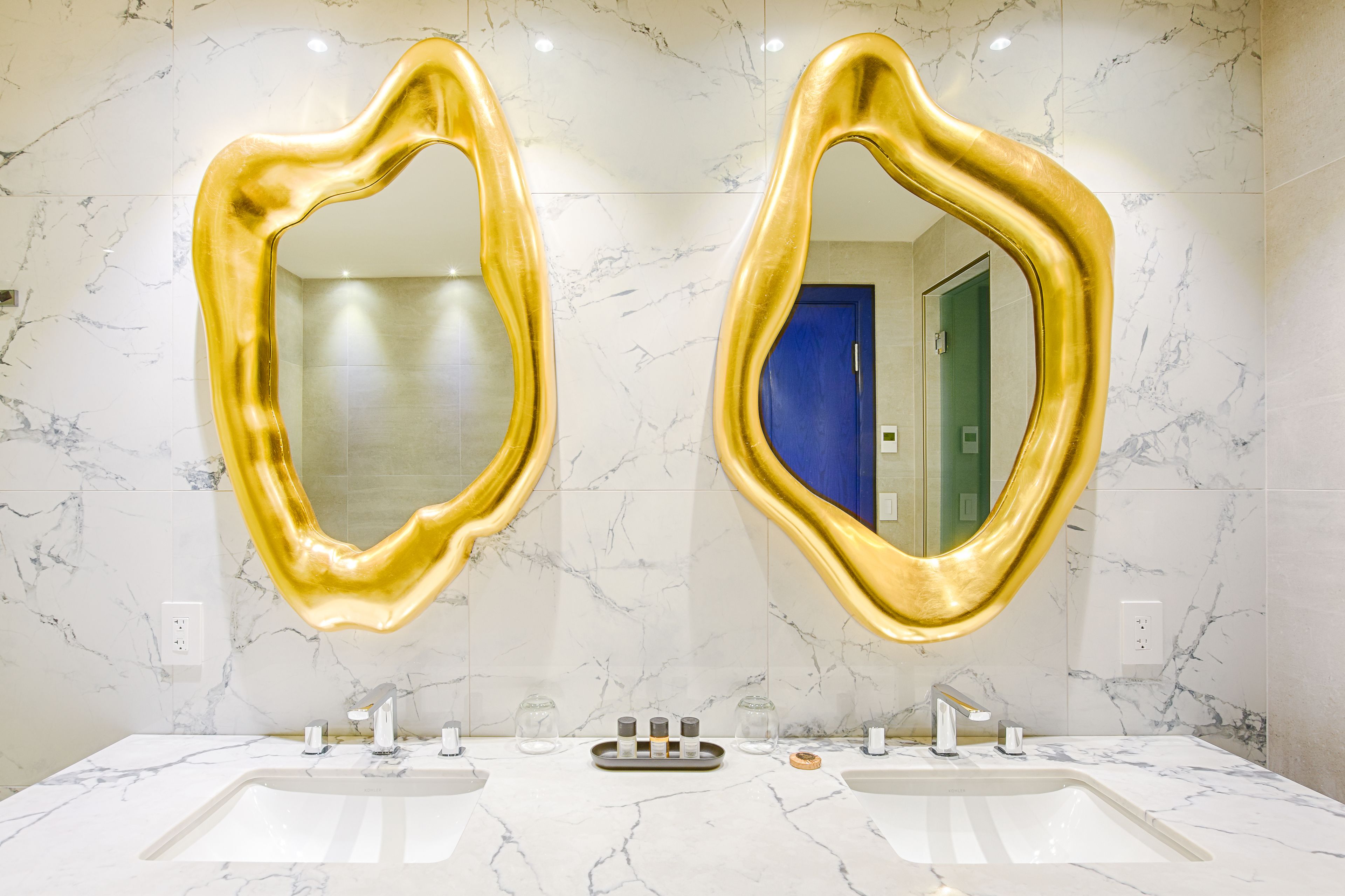A bathroom with two sinks, marble walls, and golden mirrors.
