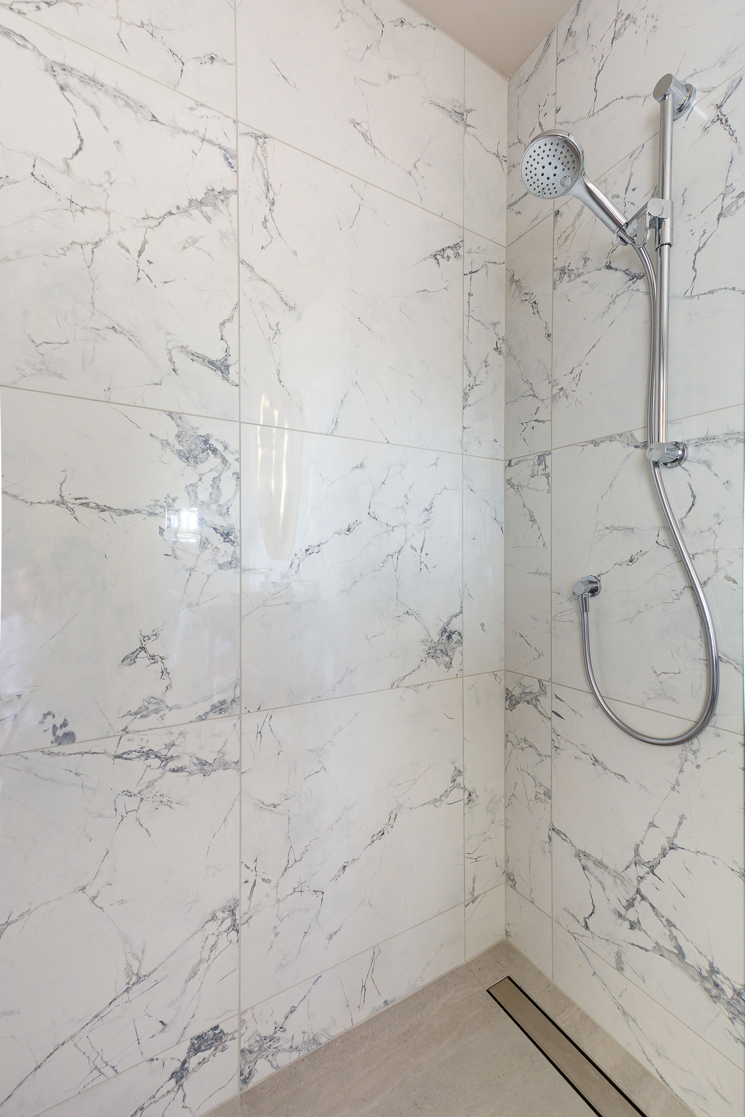 Un baño con zócalos de mármol blanco y ducha con cabezal de ducha manual.