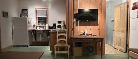 Une cuisine compacte équipée d’un réfrigérateur, d’un four à micro-ondes et d’un évier. On y trouve un bureau en bois avec une chaise, ainsi qu’un téléviseur fixé au mur.