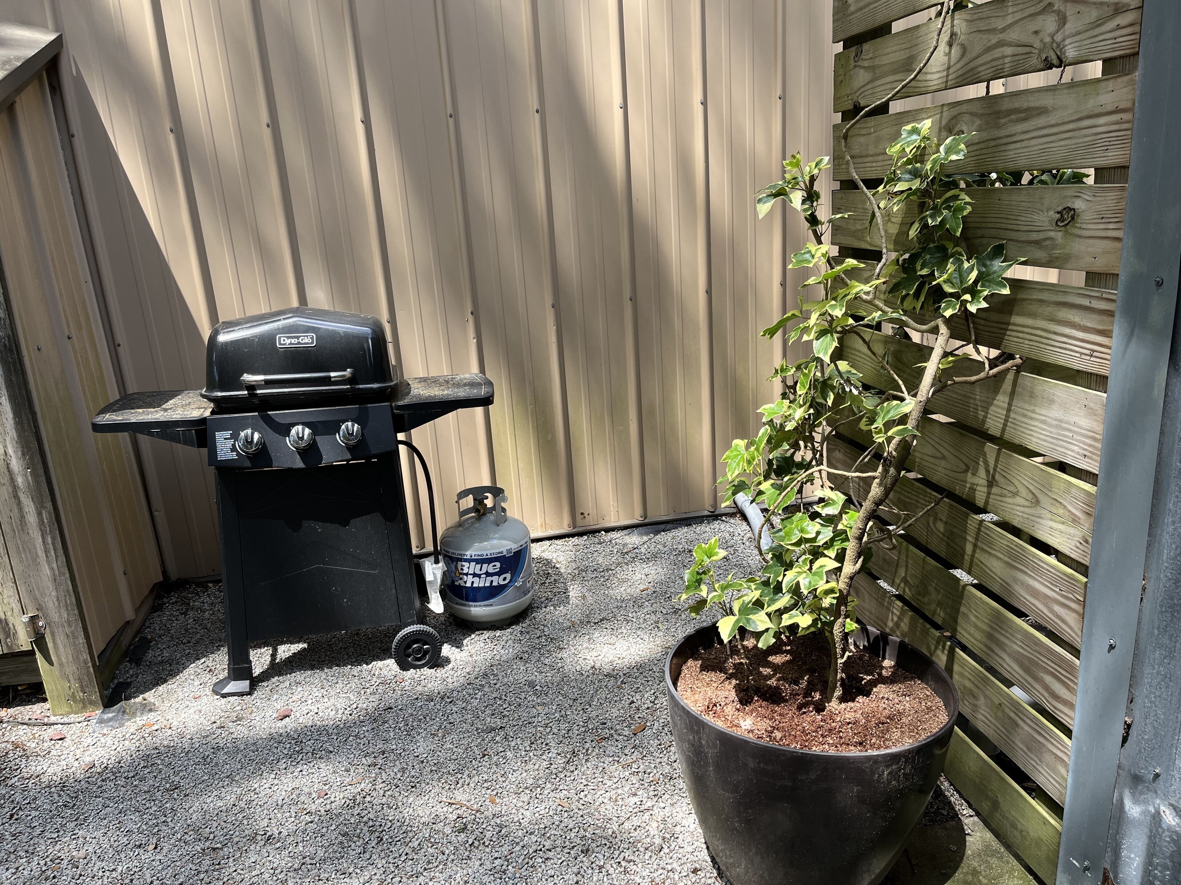 A black barbecue grill with a propane tank and a potted plant beside it.