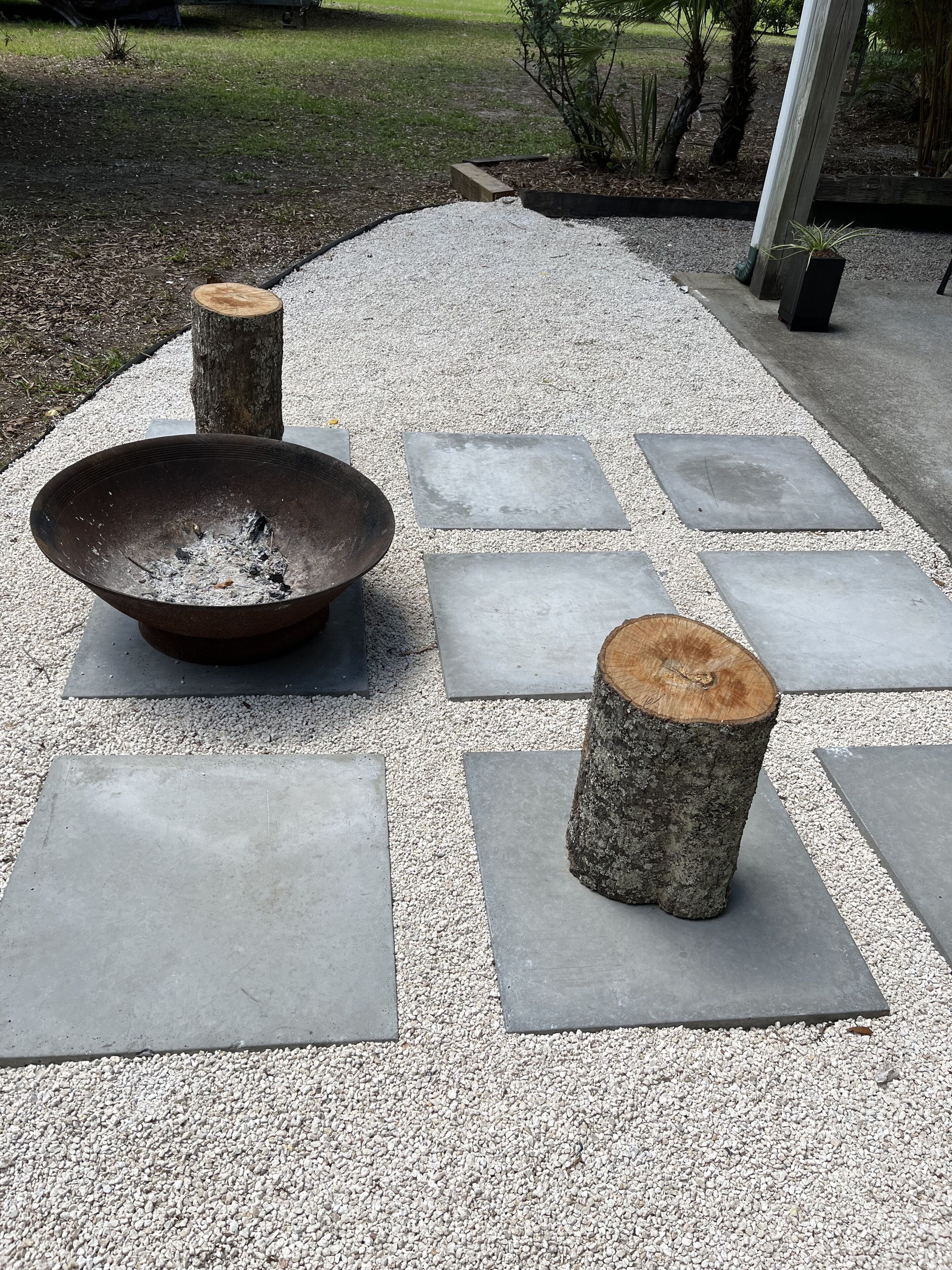 Un foyer avec un brasero et deux tabourets, entouré de dalles de pierre et de gravier.