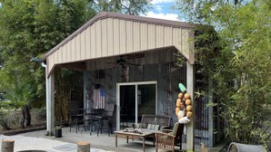 A covered patio area with a table and chairs, a fire pit, and a rustic wooden bench. - The Sleepy Shack - Private, Cozy Cottage for your next getaway! (Charleston)
