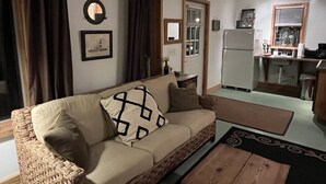A living room with a sofa, a coffee table, and a kitchen area visible through an open door. - The Sleepy Shack - Private, Cozy Cottage for your next getaway! (Charleston)