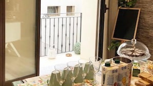 A breakfast setup with croissants, juice cartons, and glasses on a table by a window with a view of a balcony and a building. - Isolabella B&B (Mazara del Vallo)