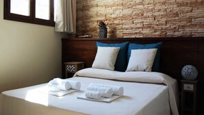 A neatly made bed with white linens and rolled towels, a wooden headboard, and a stone wall backdrop. - Isolabella B&B (Mazara del Vallo)