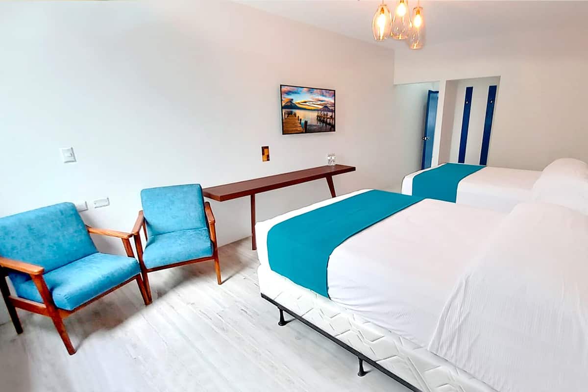 A hotel room with two beds, a desk, and two blue chairs.