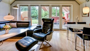 A modern living room with a leather sofa, a dining table, and a large window with a view of the outdoors. - Child-friendly thatched cottage on a large plot. Natural property from private owner (Fereininsel Römö)