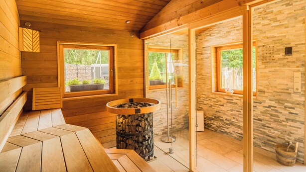 A wooden cabin interior with a sauna, wooden benches, and large windows. - Cozy round log villa with SwimSpa, whirlpool and sauna (Hellenthal)