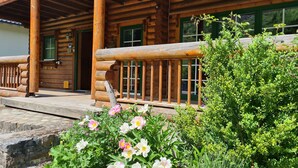 A wooden log cabin with a porch, green shutters, and a stone pathway leading to the entrance. - Cozy round log villa with SwimSpa, whirlpool and sauna (Hellenthal)