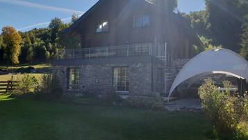 A two-story house with a stone facade, a balcony, and a large white tent-like structure in the yard.