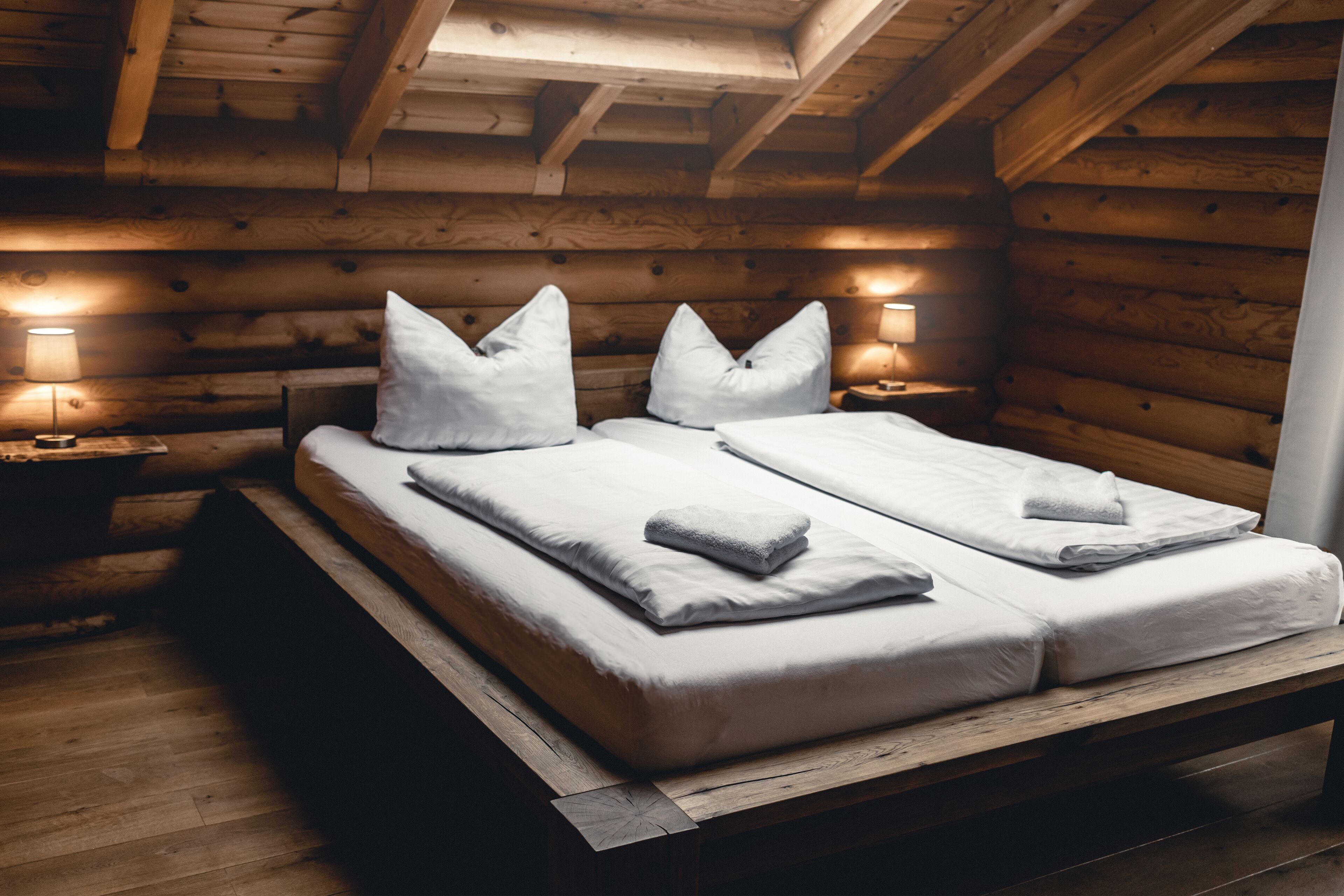 A wooden cabin-style room with a bed and two bedside tables, each with a lamp.