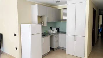 Una cocina compacta con gabinetes blancos, un microondas integrado y un refrigerador.