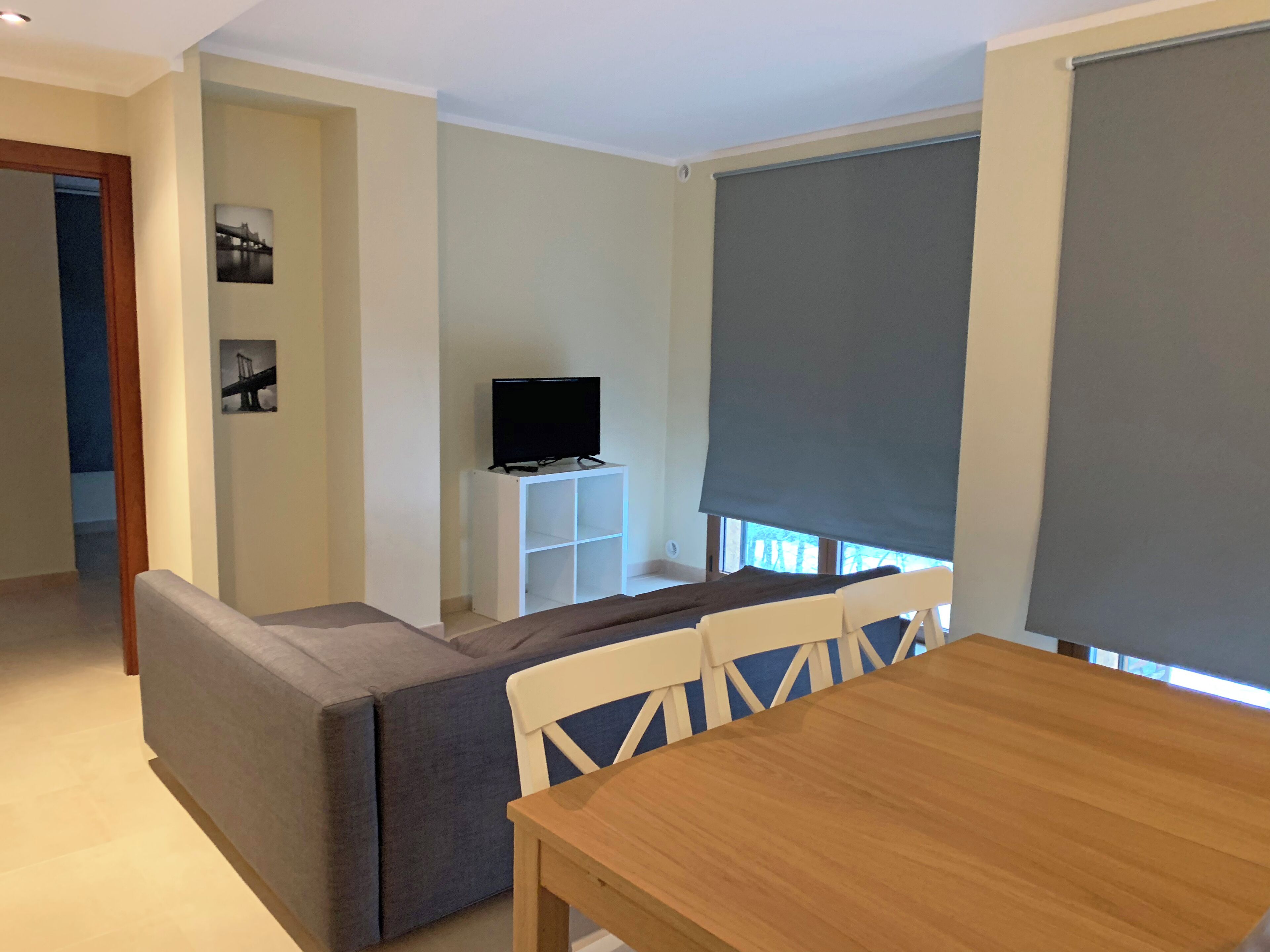 A modern living room with a sofa, a wooden dining table, and a TV on a white stand.