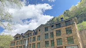 A multi-story building with a stone facade, large windows, and balconies. - Apartamentos Llorts Ordino 3000 (La Cortinada)