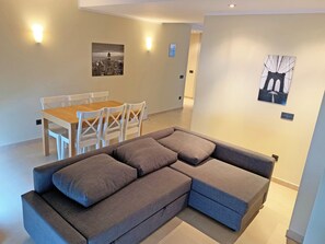 Una sala de estar moderna con un sofá seccional gris, una mesa de comedor de madera con sillas blancas y dos lámparas de pared.