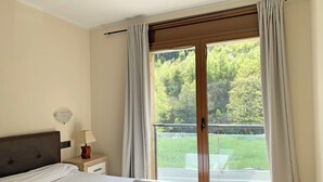 A hotel room with a bed, a nightstand, a lamp, and a view of a green landscape through a sliding glass door. - Apartamentos Llorts Ordino 3000 (La Cortinada)