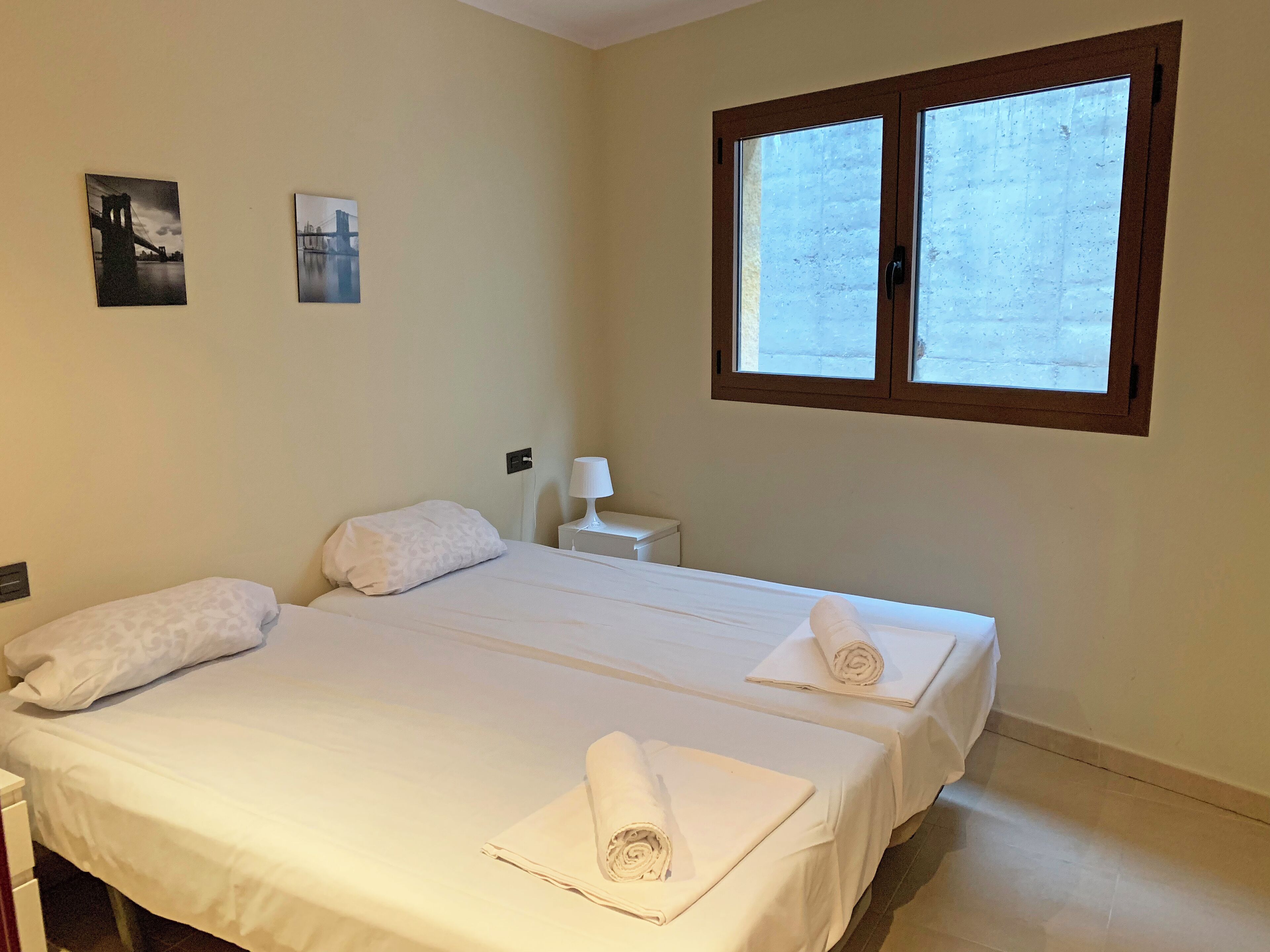 A hotel room with two beds, a nightstand, a lamp, and two framed pictures on the wall.