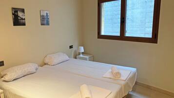A hotel room with two beds, a nightstand, a lamp, and two framed pictures on the wall.