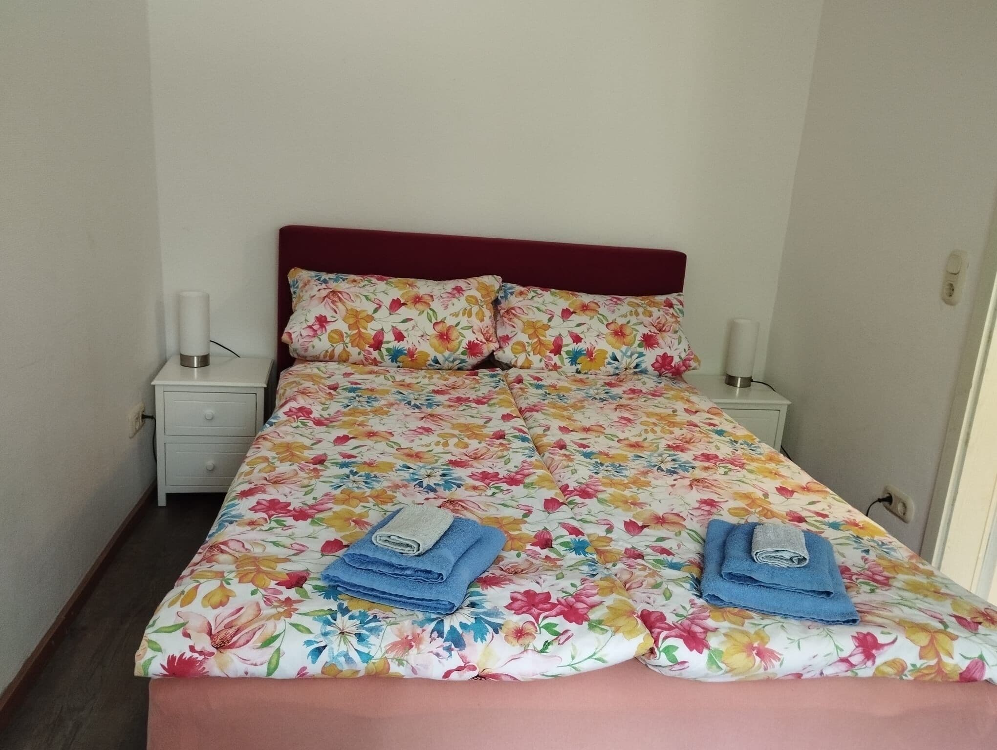 A bed with a floral bedspread, two pillows, and two folded towels.