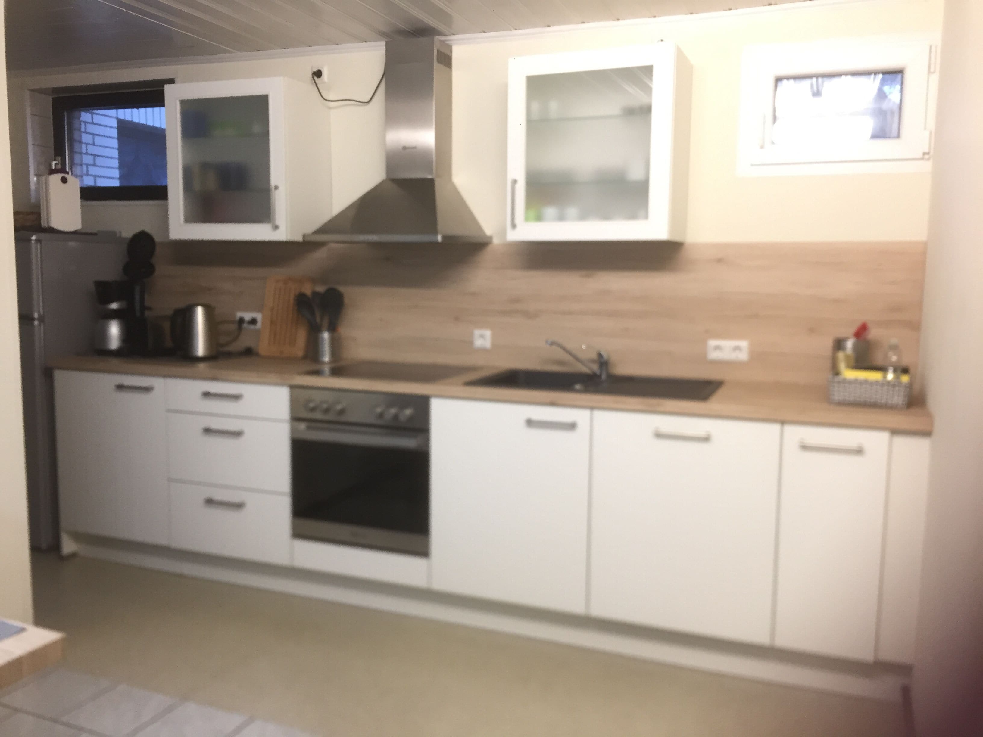 A modern kitchen with white cabinets, a stainless steel range hood, a double sink, and a built-in oven.