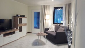 Una sala de estar moderna con un televisor de pantalla plana, un sofá, una mesita de centro y un jarrón decorativo.