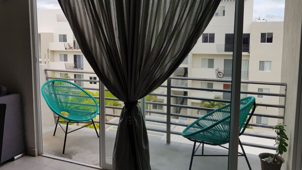 Un balcón con dos sillas verdes, una planta en maceta y vistas a edificios residenciales.