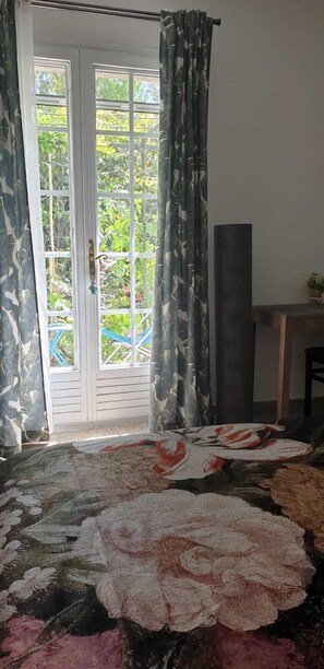 A room with a large bed, a sliding glass door leading to a balcony, and a small table with a plant.