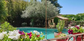 A pool surrounded by lush greenery and a stone building with a tiled roof.