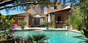 A pool area with lounge chairs, a covered seating area, and potted plants. - Villa Solary (Le Pontet)