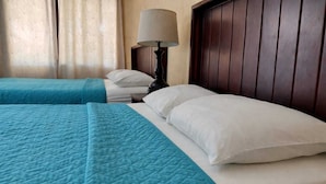 A hotel room with two beds, each with a blue quilted bedspread and white pillows. There is a wooden headboard and a bedside table with a lamp. - Hotel La Colonia (San Sebastian)