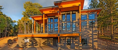 A modern two-story house with large windows and a wooden deck.