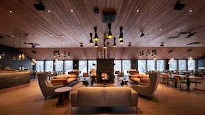 A spacious lobby with a central fireplace, multiple seating areas, and a wooden ceiling. - Northern Lights Village Levi (Kittila)