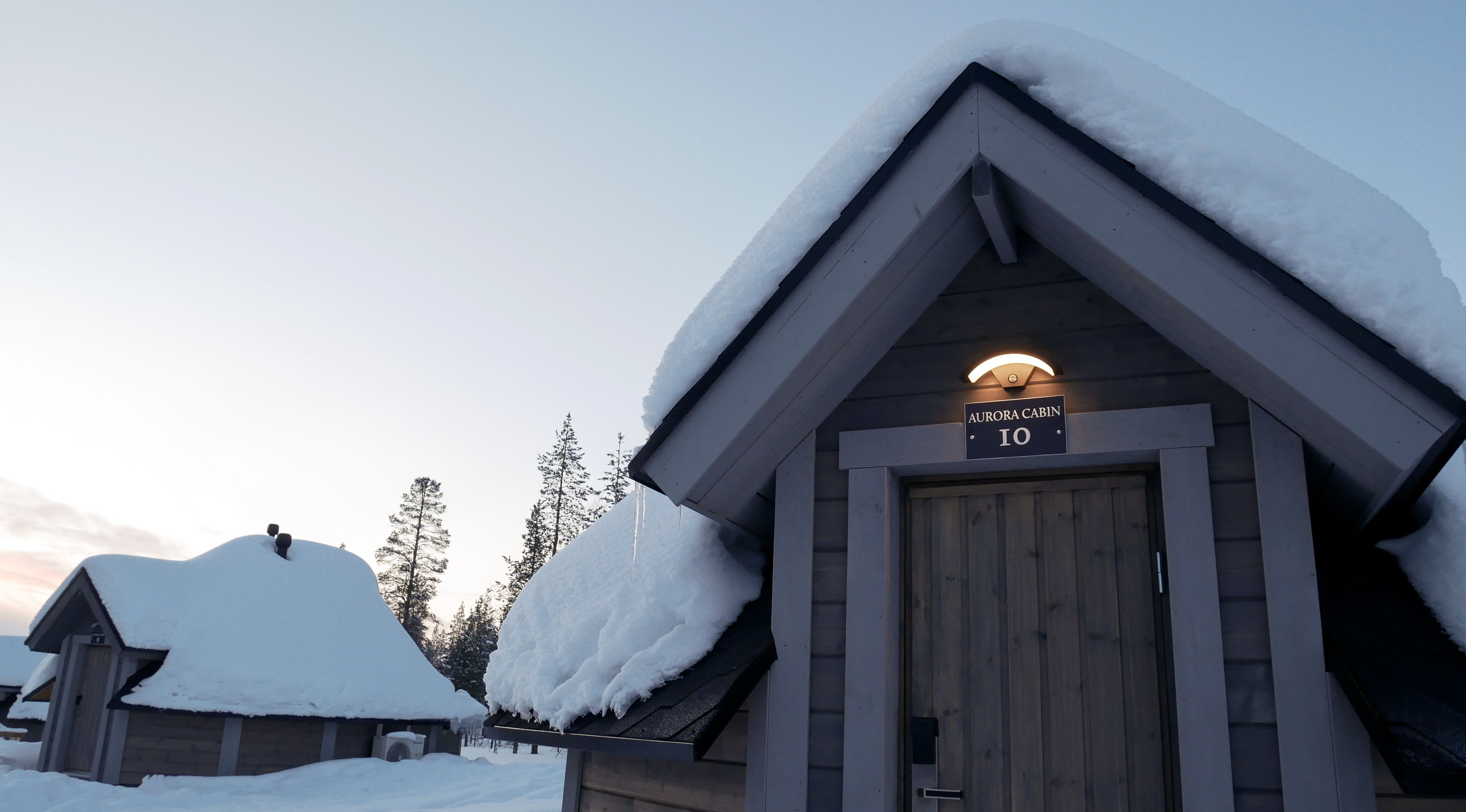 A cabin labeled "Aurora Cabin 10" with a snow-covered roof and a wooden door.