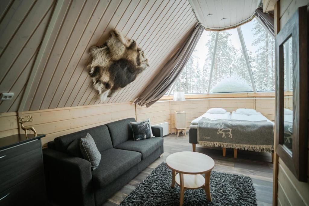 A cozy room with a large fur rug, a sofa, a round table, and a bed with a blanket featuring animal prints.