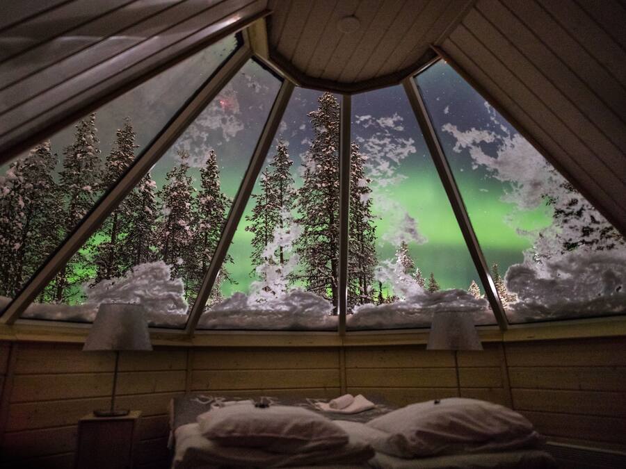 Ein Zimmer mit einem Bett und einem Fenster mit Blick auf Bäume und das Polarlicht.