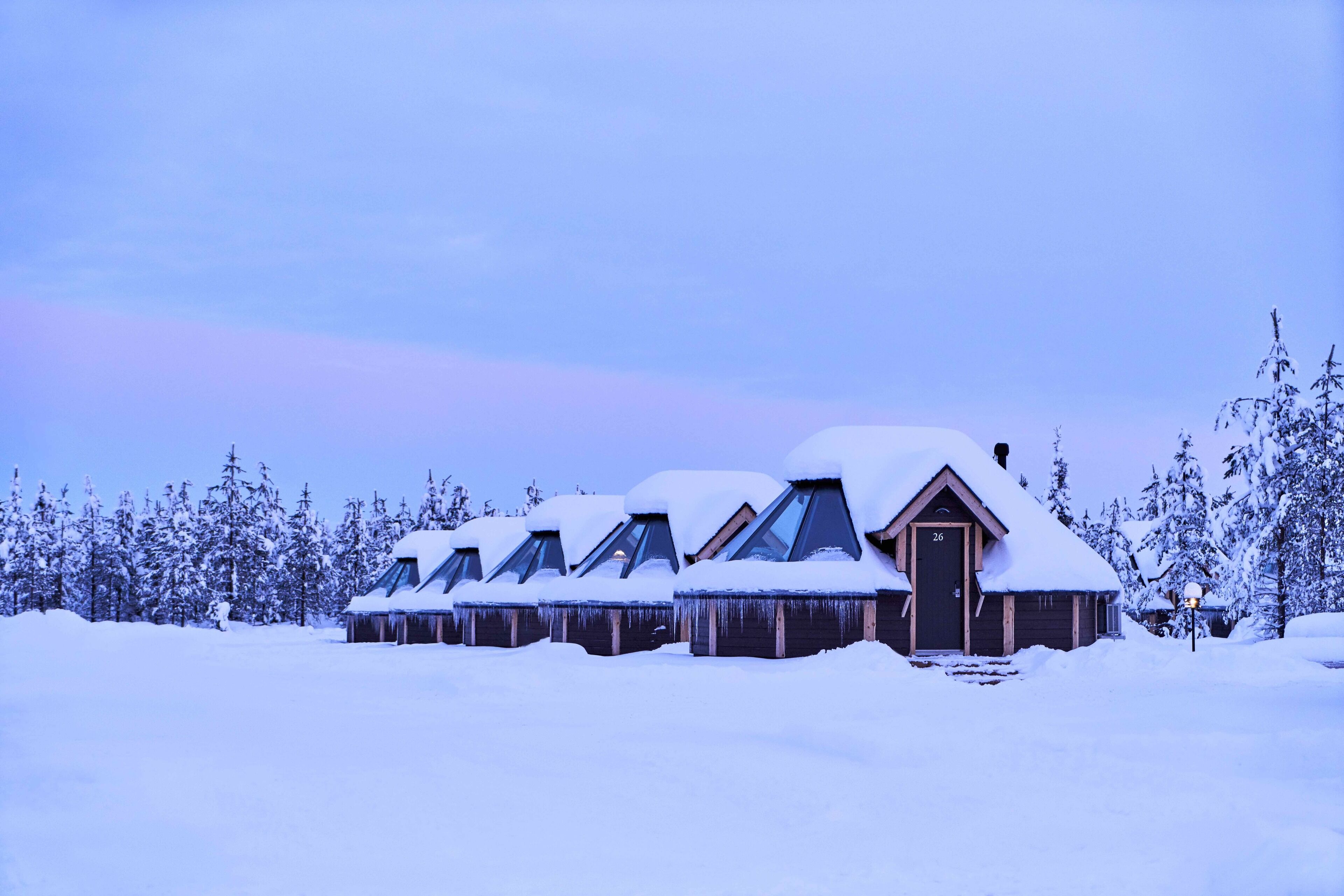 A row of log cabins covered in snow, with a clear sky in the background.