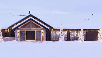 A log cabin with a snow-covered roof and a large front door, surrounded by snow-covered trees.