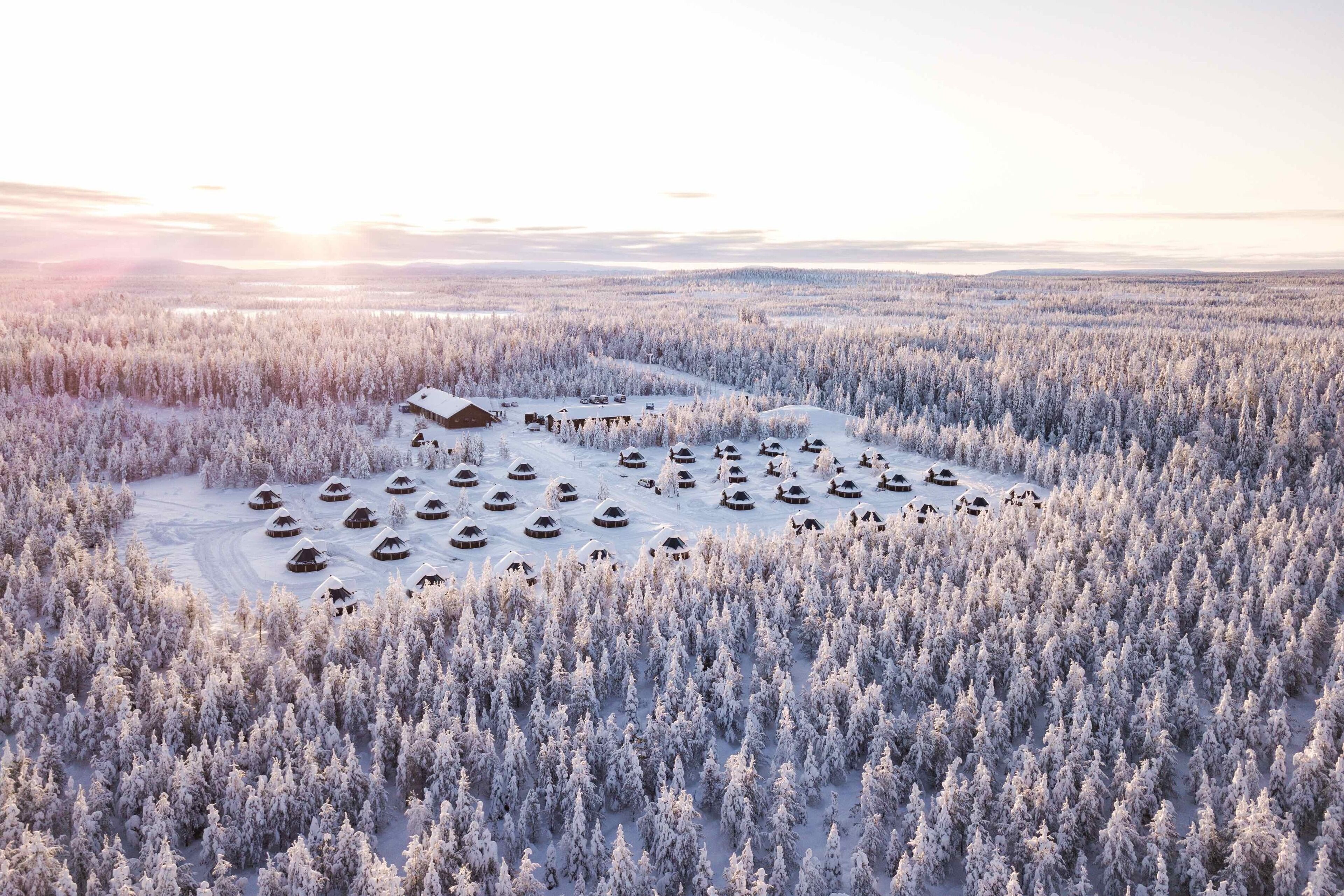 An aerial view of a snow-covered forest with several yurts and a large building.