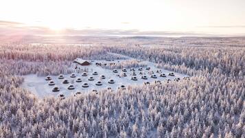 An aerial view of a snow-covered forest with several yurts and a large building.