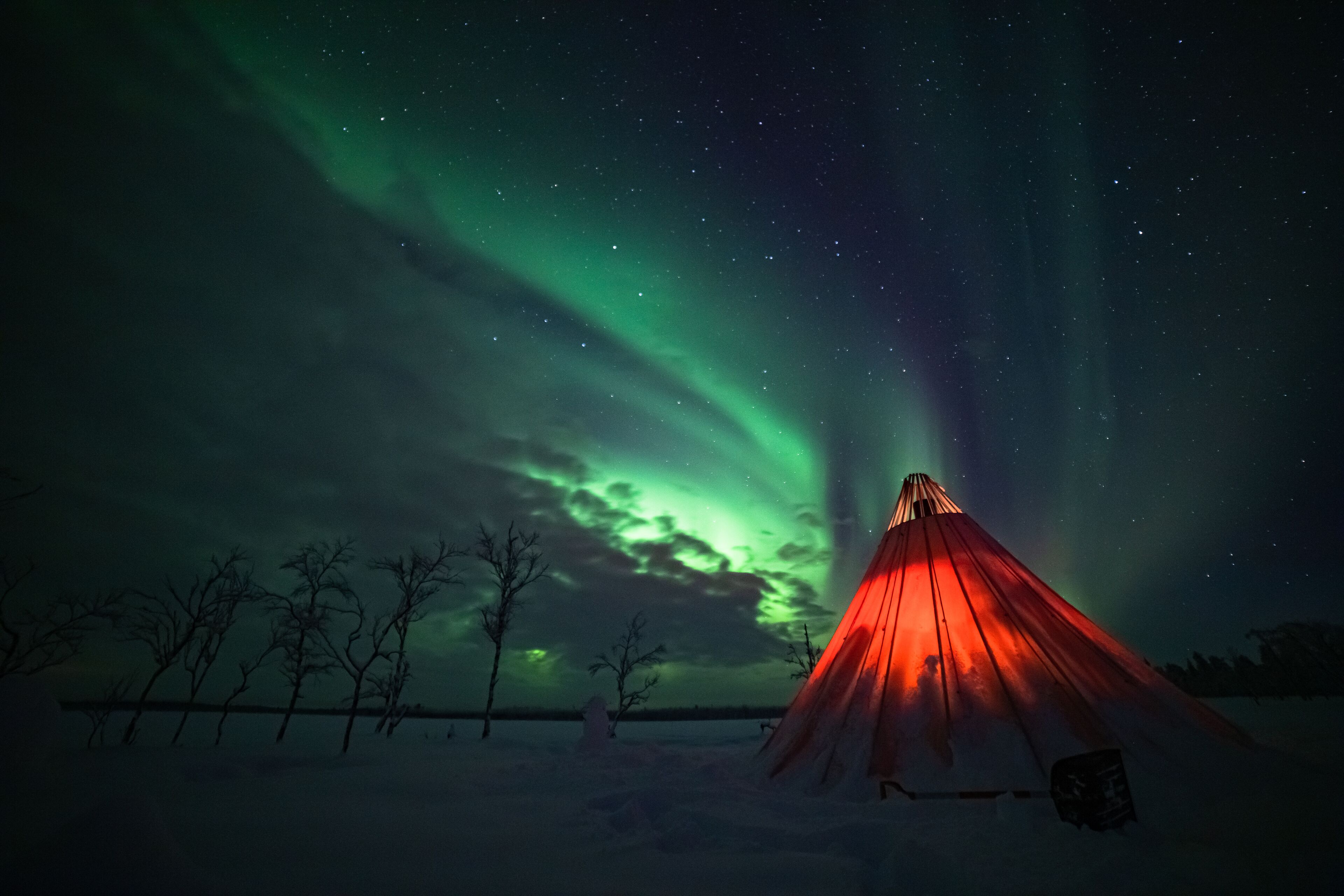 A snow-covered landscape with a red tent in the foreground and the Northern Lights in the background.