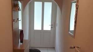 Een gang met een standbeeld, een zwarte mat, een radiator en een witte deur met ramen.