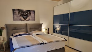 Een moderne slaapkamer met een groot bed, een hoofdbord, een nachtkastje met een vaas en een wanddecoratie.