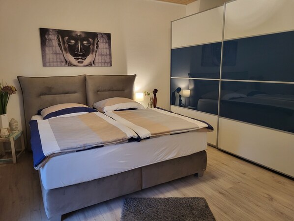 Un dormitorio moderno con una cama grande, un cabecero, una mesita de noche con un florero y una obra de arte colgada en la pared.