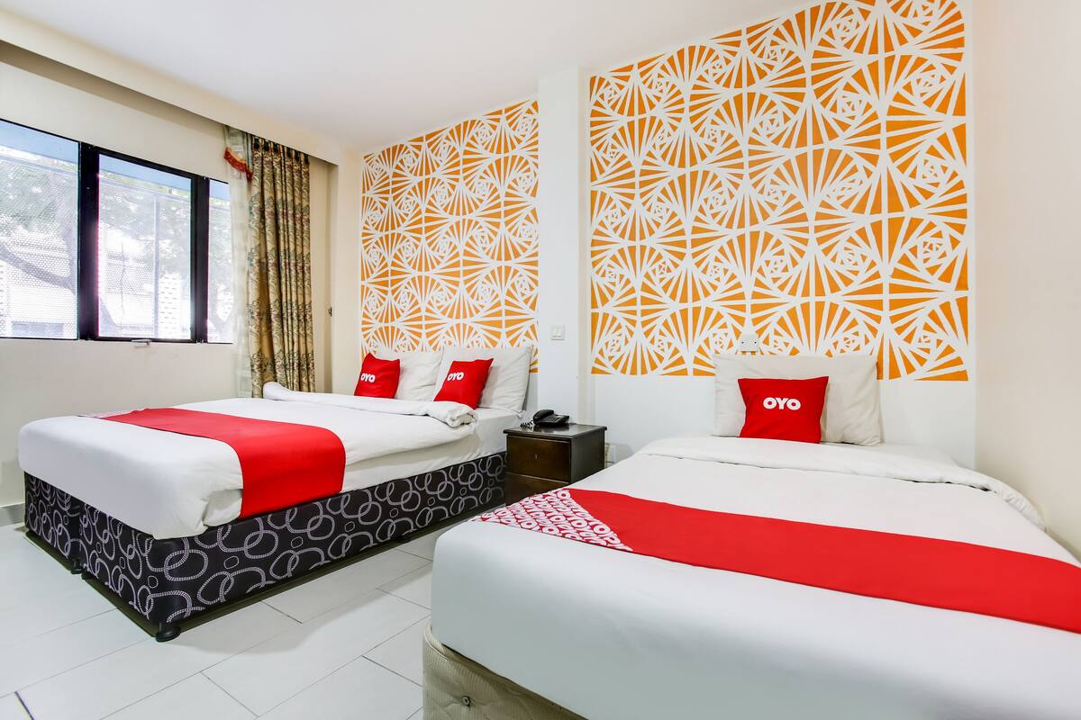 A hotel room with two beds, each with a red and white bedspread, and a patterned headboard.
