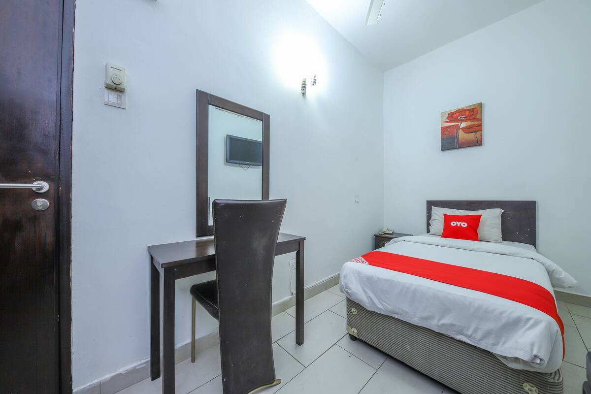 A hotel room with a bed, a desk, a chair, a television, and a painting on the wall.