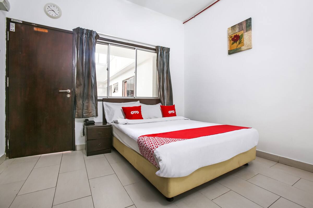 A bedroom with a bed, a nightstand, a wooden door, and a window with curtains.