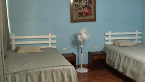 Una habitación con dos camas, un ventilador de pie y un cuadro en la pared.