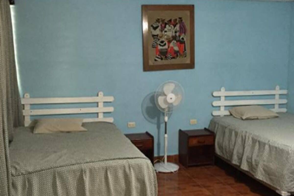 A room with two beds, a standing fan, and a framed picture on the wall.