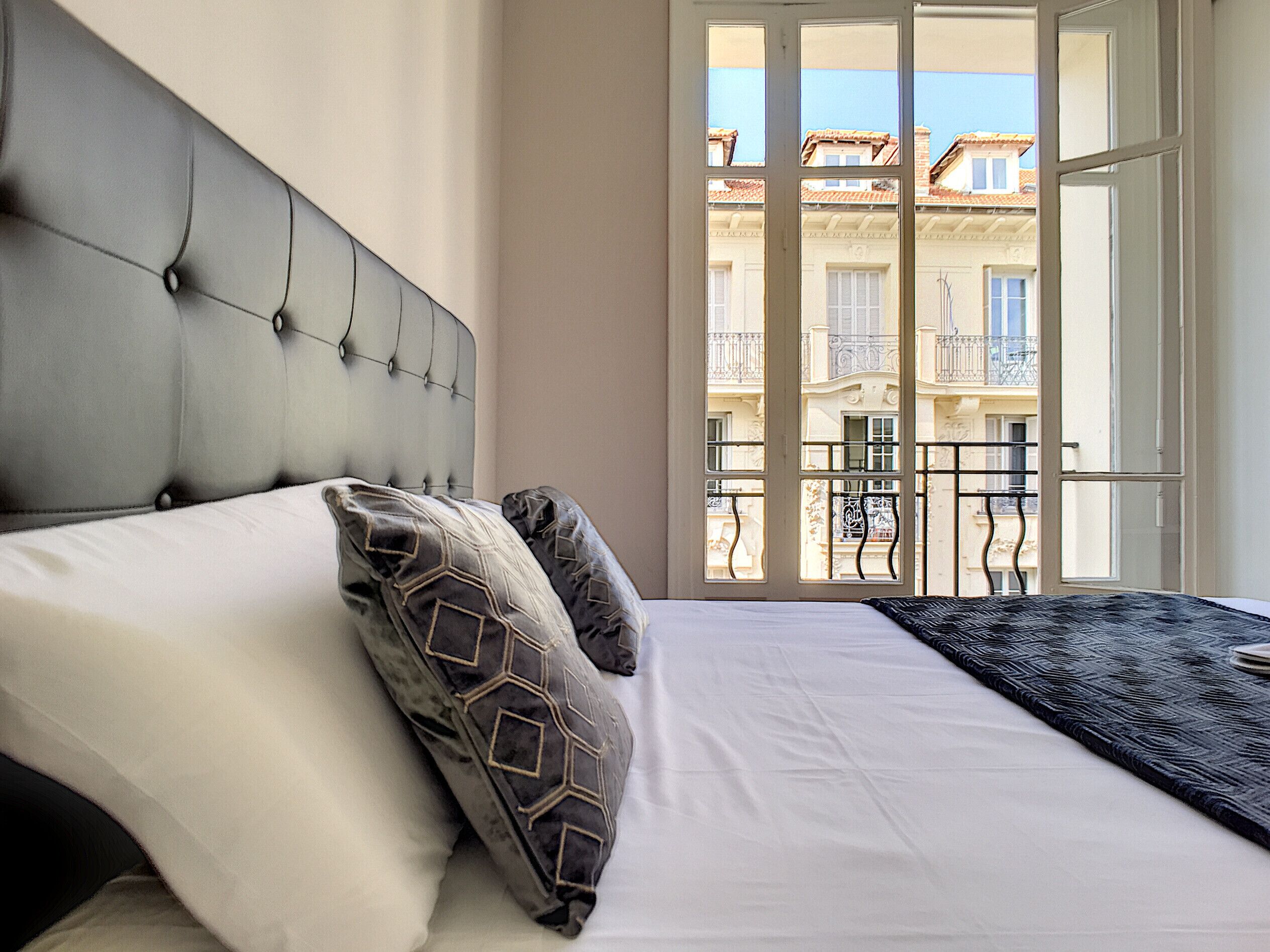 A bedroom with a large bed, a headboard, and a view of balconies through a window.