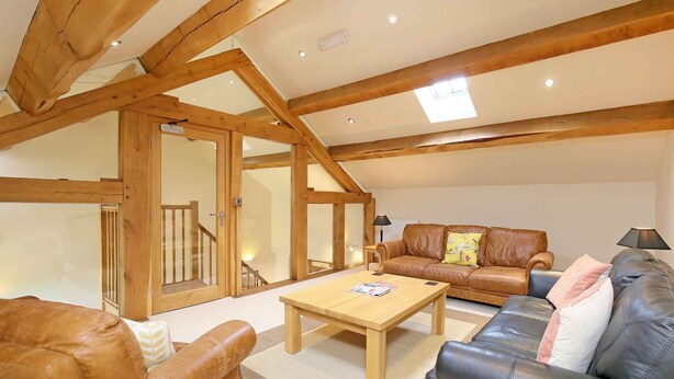 A spacious living room with a high ceiling and exposed wooden beams, featuring a brown leather sofa, a black leather sofa, and a wooden coffee table. - Cold Cotes Guest House (Harrogate)